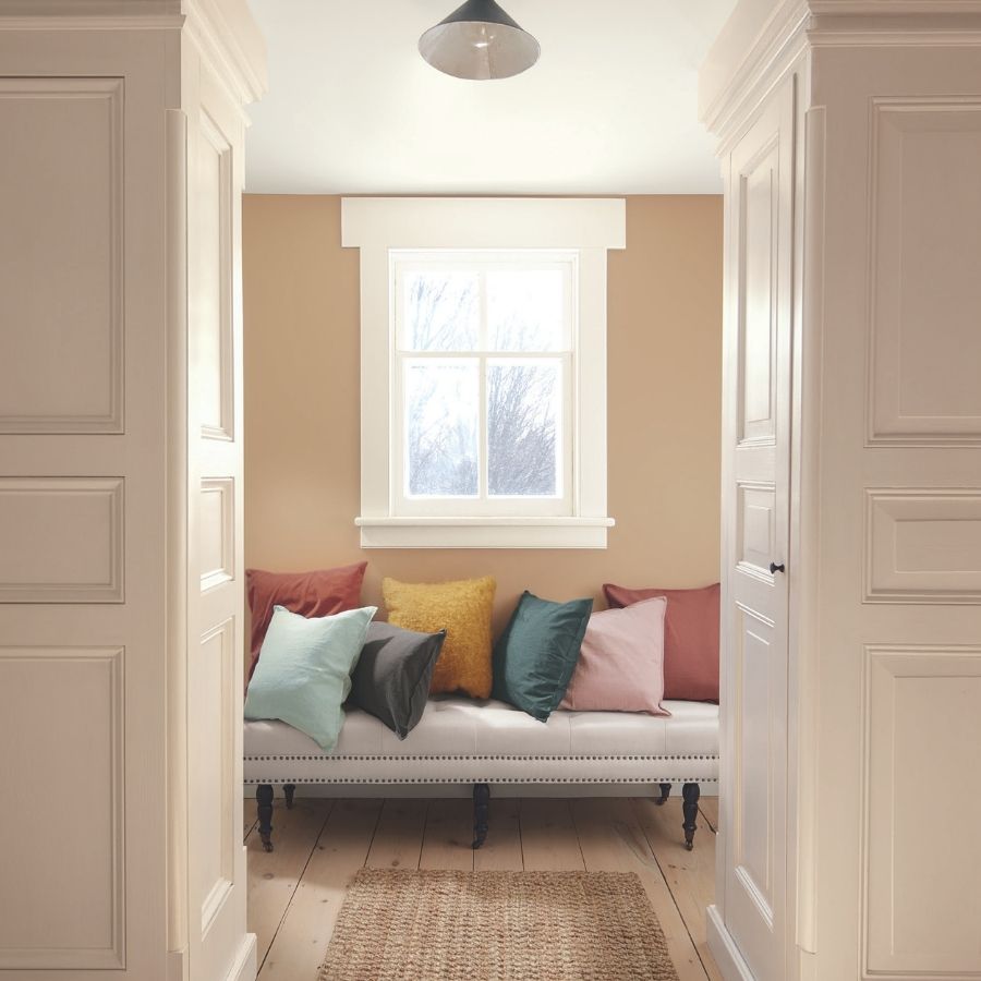 Nook with colorful pillows on a bench by a window wall color is Benjamin Moore's Sherwood Tan 1054